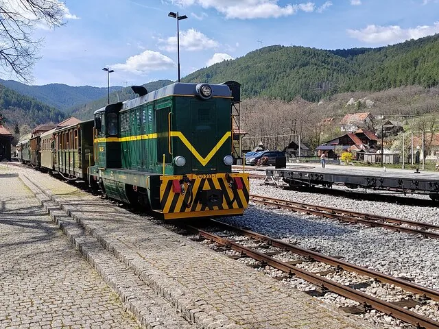 Groene historische trein op een spoorlijn in een bergachtig gebied.